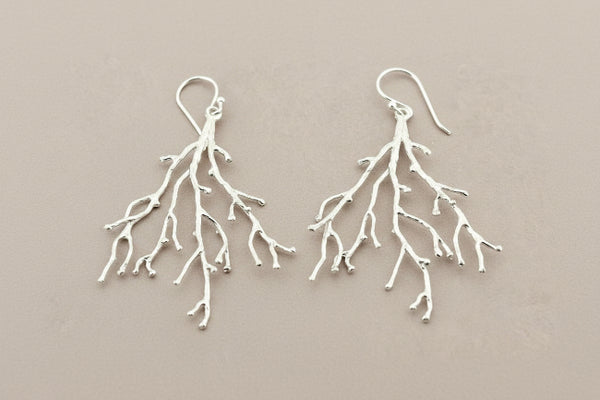 Silver branch-like earrings on a gray background