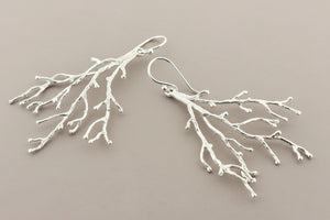 Silver branch-like earrings on a dark gray background