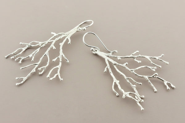 Silver branch-like earrings on a dark gray background