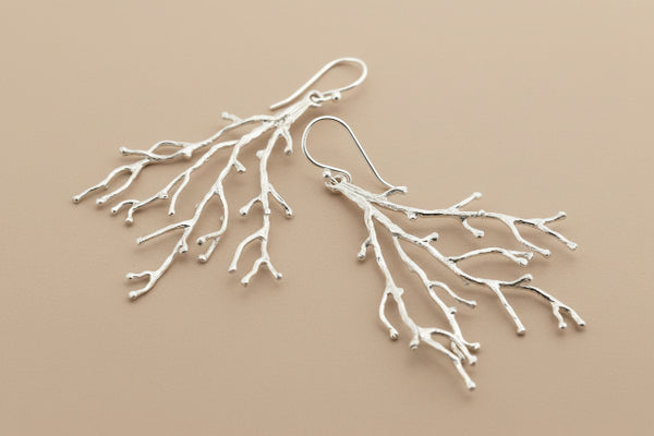 Silver branch-like earrings on a dark gray background