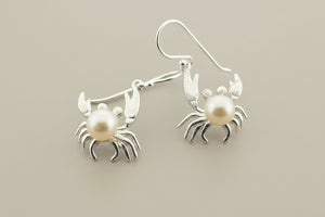 Silver crab earrings with pearl centers on a gray background