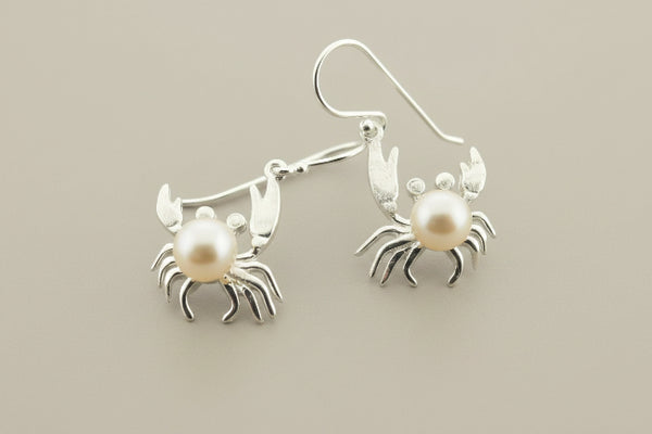 Silver crab earrings with pearl centers on a gray background
