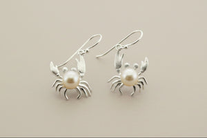 Silver crab earrings with pearl centers on a gray background