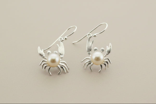 Silver crab earrings with pearl centers on a gray background