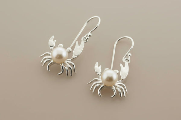 Silver crab earrings with pearl centers on a dark gray background