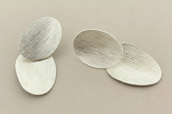 Pair of silver oval earrings on a dark gray background