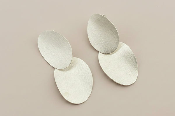 Pair of silver oval earrings on a gray background