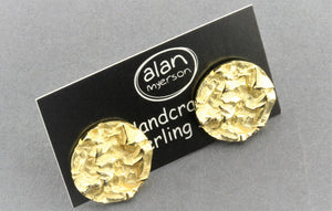 A pair of textured gold round stud earrings mounted on a black display card with the brand name 'alan myerson' visible, set against a neutral gray background.