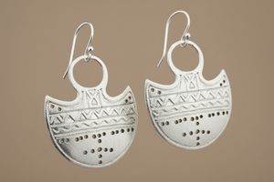 Pair of silver earrings with intricate patterns on a brown background