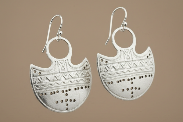 Pair of silver earrings with intricate patterns on a brown background