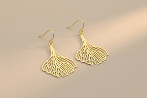Gold leaf-shaped earrings on a gray background